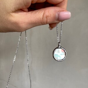 May include: A silver chain necklace with a round, iridescent pendant. The pendant has a textured, irregular edge.