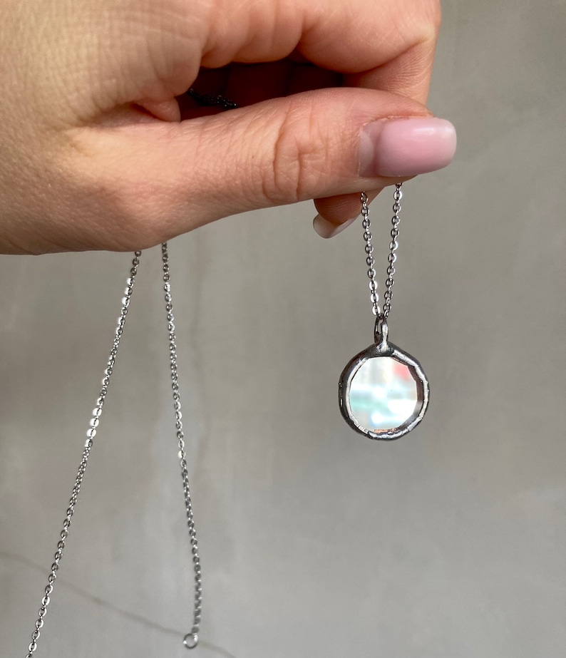 May include: A silver chain necklace with a round, iridescent pendant. The pendant has a textured, irregular edge.