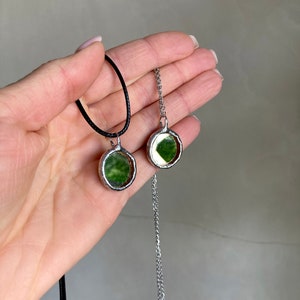 May include: Two silver necklaces with round green glass pendants. One necklace has a black cord and the other has a silver chain.