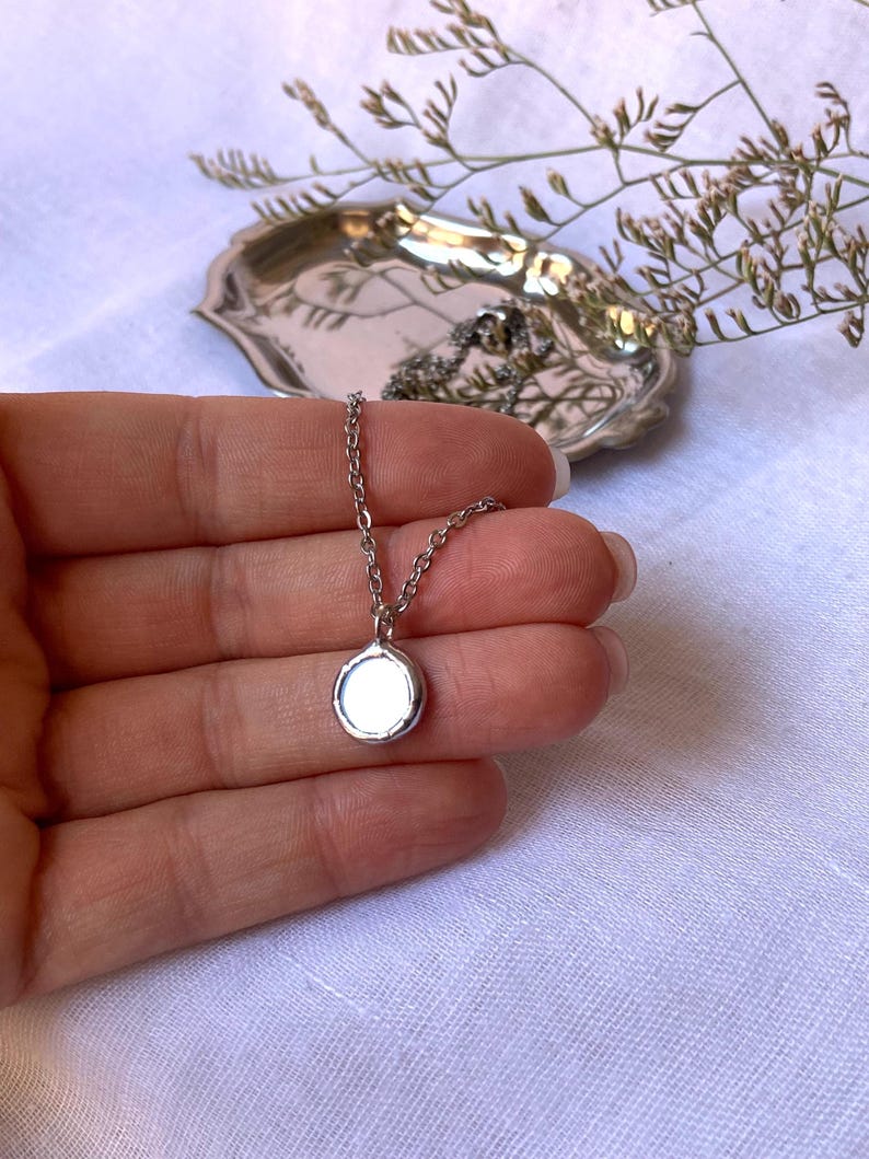 May include: A silver chain necklace with a small, round, silver pendant.