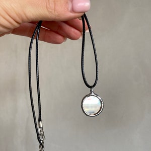 May include: A silver pendant necklace with a round, iridescent glass charm. The necklace is on a black cord with a silver chain extension.