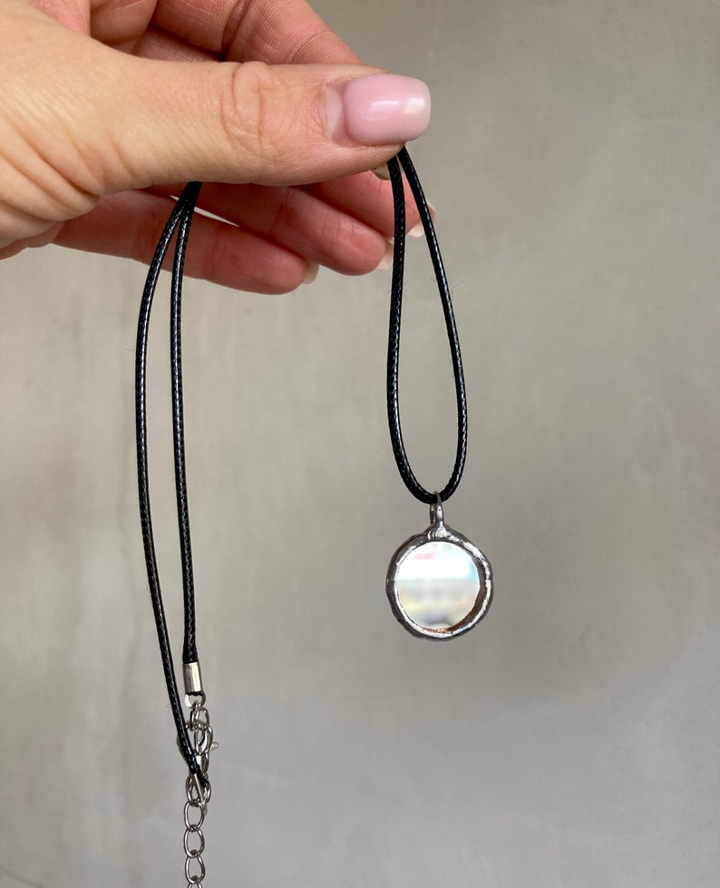May include: A silver pendant necklace with a round, iridescent glass charm. The necklace is on a black cord with a silver chain extension.