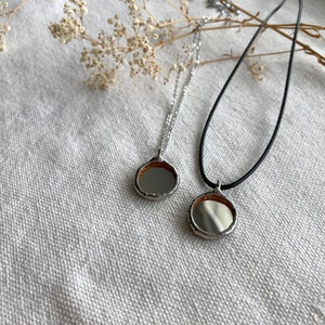 May include: Two silver necklaces with round, mirrored pendants. One necklace has a black cord and the other has a silver chain.