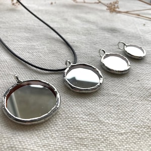 Peut inclure: Quatre pendentifs ronds en miroir argentés de tailles différentes. Le plus grand pendentif est attaché à un collier en cordon noir.