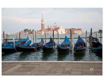 Puede incluir: Una fila de góndolas azules están atracadas en un canal de Venecia, Italia. Las góndolas están alineadas en una fila, con el agua reflejando el cielo y los edificios en el fondo. Las góndolas son un medio de transporte popular en Venecia.