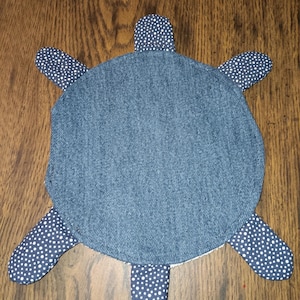 Puede incluir: Un artículo en forma de tortuga de mezclilla con cuatro apéndices en forma de aleta. El cuerpo de la tortuga es de mezclilla azul liso, mientras que las aletas son de tela azul marino con lunares blancos. Probablemente sea una pieza decorativa o un juguete.