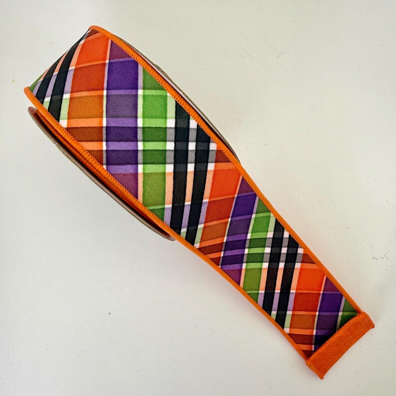 May include: A roll of decorative ribbon with a plaid pattern in orange, purple, green, and black. The ribbon has an orange border and is likely used for crafts or gift wrapping.