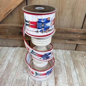 May include: A spool of white wired ribbon featuring a repeating pattern of nutcracker figures in blue and red uniforms against a faint musical score background. The ribbon edges are finished with a thin, vibrant red stitched border.