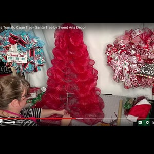 May include: A woman is making a red mesh tomato cage Christmas tree. The tree is decorated with red and white ribbon and a sign that says "Merry Christmas".