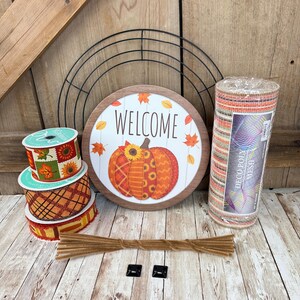 May include: A collection of fall-themed craft supplies. Includes a round wooden sign with a pumpkin design and the word "WELCOME", rolls of ribbon, deco mesh, pipe cleaners, and mounting hardware. The color palette features orange, brown, and green.