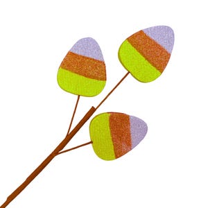 May include: A decorative branch featuring three candy corn-shaped ornaments. Each ornament has a glittery finish with horizontal bands of light purple, orange, and bright yellow. The branch is brown and has three thin stems extending to each ornament.