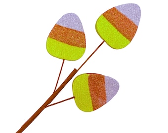 May include: A decorative branch featuring three candy corn-shaped ornaments. Each ornament has a glittery finish with horizontal bands of light purple, orange, and bright yellow. The branch is brown and has three thin stems extending to each ornament.