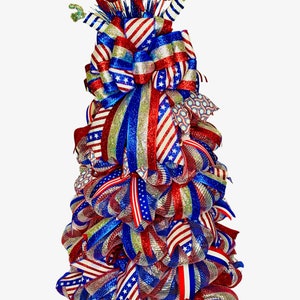 May include: A red, white, and blue patriotic wreath with a large bow and glitter accents. The wreath is made of mesh and ribbon and features a star pattern.