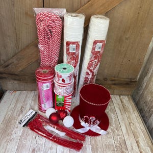 May include: A collection of holiday craft supplies including a red and white rope, two rolls of white mesh, a roll of red and white striped mesh, a spool of candy cane ribbon, a box of 100 mini lights, three ornaments, and red chenille stems.