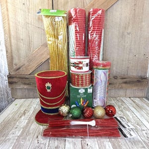May include: A collection of holiday craft supplies including a red velvet top hat, gold tinsel, two rolls of red deco mesh, two spools of ribbon with nutcracker and gold patterns, a box of 100 multicolor LED mini lights, ornaments, and red chenille stems.