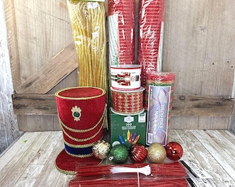 May include: A collection of holiday craft supplies including a red velvet top hat, gold tinsel, two rolls of red deco mesh, two spools of ribbon with nutcracker and gold patterns, a box of 100 multicolor LED mini lights, ornaments, and red chenille stems.