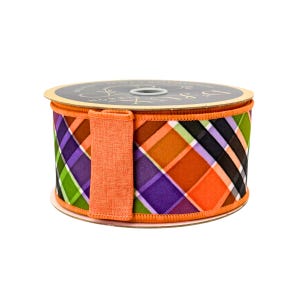 May include: A spool of decorative ribbon with a plaid pattern in orange, purple, green, and black. The ribbon has an orange fabric loop attached to the side. The spool is on a white background.