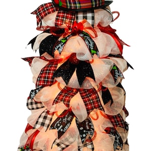 May include: A white mesh Christmas tree with red and black plaid ribbon, black ribbon, and a black top hat with a plaid band. The tree is decorated with white lights.