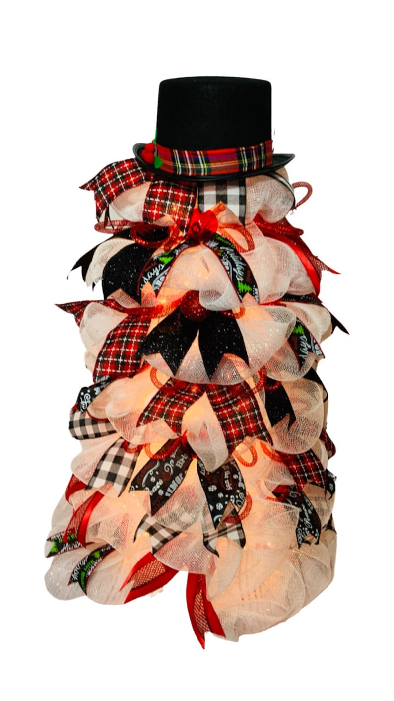 May include: A white mesh Christmas tree with red and black plaid ribbon, black ribbon, and a black top hat with a plaid band. The tree is decorated with white lights.