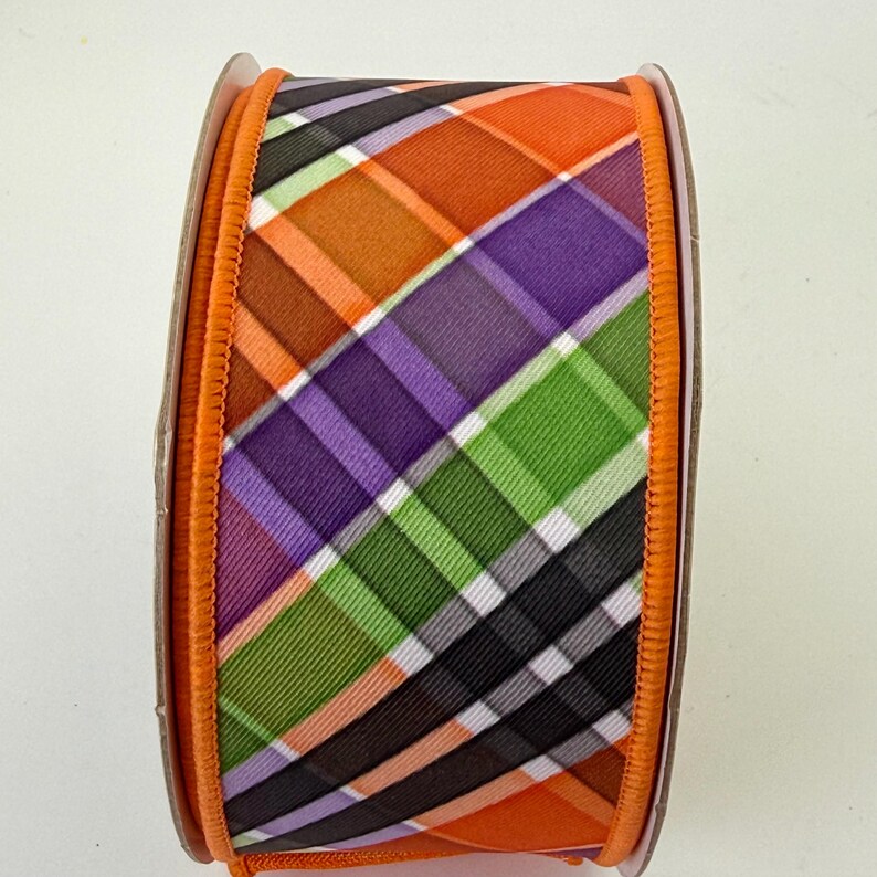 May include: A spool of decorative ribbon with a plaid pattern in orange, purple, green, black, and white. The ribbon has an orange border and is suitable for crafts and gift wrapping.