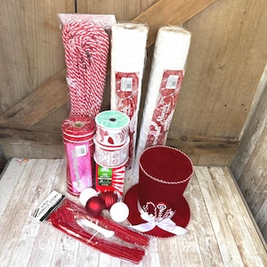 May include: A collection of craft supplies including a red and white striped rope, two rolls of white mesh, a roll of red striped mesh, two spools of patterned ribbon, a box of 100 mini lights, red and white ornaments, red chenille stems, and a red top hat.