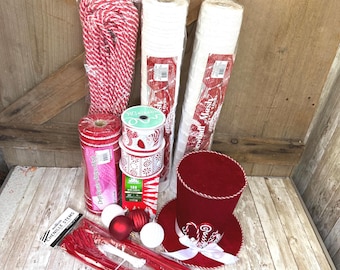 May include: A collection of craft supplies including a red and white striped rope, two rolls of white mesh, a roll of red striped mesh, two spools of patterned ribbon, a box of 100 mini lights, red and white ornaments, red chenille stems, and a red top hat.