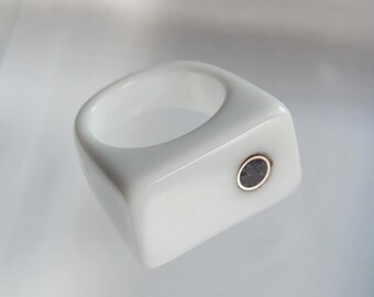 May include: A white ceramic ring with a black stone inlay. The ring is rectangular in shape and has a smooth, polished finish.