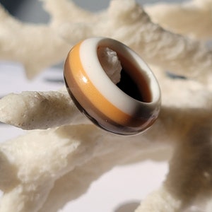 May include: A brown, orange, and white striped ring made of resin.