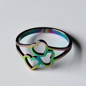 May include: A rainbow iridescent stainless steel ring with three interlocking heart cutouts.