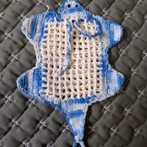 May include: Handmade crochet potholder in the shape of a stingray. The potholder features a cream-colored open weave center with blue and white striped edging. A loop is attached for hanging.
