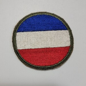 May include: A round embroidered patch with a green border and a tri-color design of blue, white, and red.