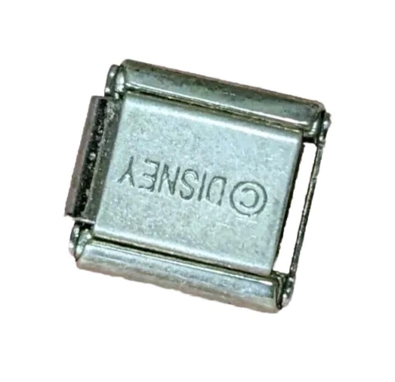 Puede incluir: Un charm de metal plateado con la palabra "DISNEY" y un s&iacute;mbolo de copyright.