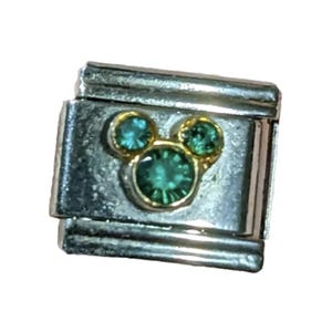 Puede incluir: Un charm para pulsera de plata con un dise&ntilde;o de cabeza de Mickey Mouse en oro con tres diamantes de imitaci&oacute;n verdes.