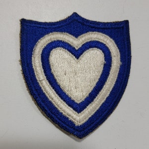 May include: A blue and white embroidered patch in the shape of a shield with a white heart inside. The heart has two white outlines.