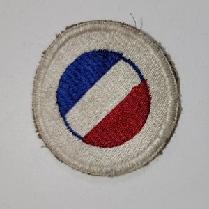 May include: A white, round, embroidered patch with a blue, white, and red circle design. The circle is divided into three sections: a blue half-circle, a white half-circle, and a red half-circle.