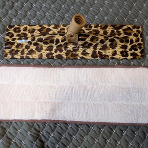 May include: A rectangular mop head with a leopard print design and a separate white microfiber pad with a brown border. The mop head has a beige plastic connector.