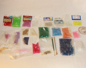 May include: Assortment of colorful beads in various sizes and shapes, packaged in clear plastic bags. The beads are arranged in rows on a white surface. Some bags have labels with product information.