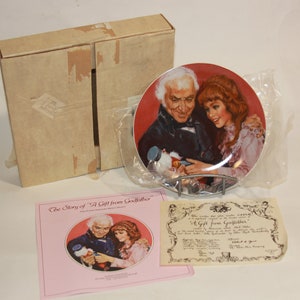 May include: A porcelain collector's plate featuring a painting of an older man and a young woman. The plate is in a box with a certificate of authenticity. The text on the certificate reads "A Gift from Godfather".