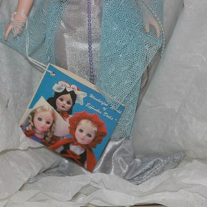 May include: A vintage doll box with a blue and silver dress and a label that reads "Wonderland World of Effanbee Dolls". The box also features a picture of three dolls with different hairstyles and outfits.