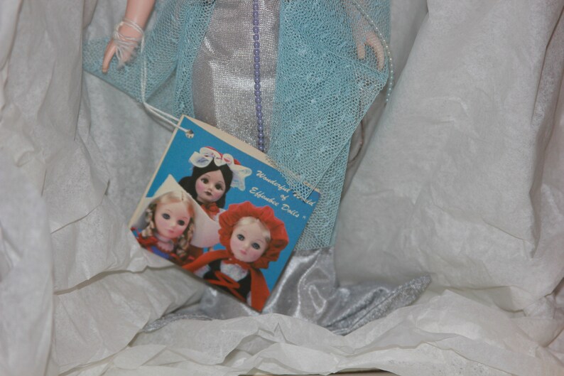 May include: A vintage doll box with a blue and silver dress and a label that reads "Wonderland World of Effanbee Dolls". The box also features a picture of three dolls with different hairstyles and outfits.