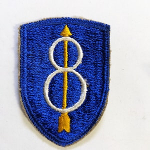May include: A blue and gold military patch with the number 8 inside two white circles and an arrow pointing up.