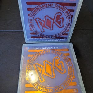 May include: Two sealed Micro Tournament Game Pack boxes. The boxes are purple with orange and red text. The text reads "100% Authentic" and "The World Pog Federation". Each pack contains 24 Pog milkcaps, 2 kinis, and a guidebook.