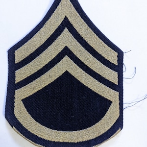 May include: A dark blue military rank patch with three gold chevrons and a gold border.