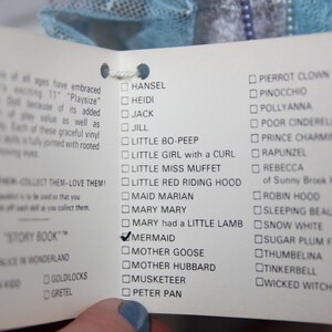 May include: A white card with a checklist of various characters, including Hansal, Heidi, Jack, Jill, Little Bo-Peep, Little Girl with a Curl, Little Miss Muffet, Little Red Riding Hood, Maid Marian, Mary Mary, Mary had a Little Lamb, Mermaid, Mother Goose, Mother Hubbard, Musketeer, Peter Pan, Pierrot Clown, Pinocchio, Pollyanna, Poor Cinderella, Prince Charming, Rapunzel, Rebecca of Sunny Brook Farm, Robin Hood, Sleeping Beauty, Snow White, Sugar Plum Fairy, Thumbelina, Tinkerbell, and Wicked Witch. The card also includes a section for "Story Book" with a checklist of Alice in Wonderland, Captain Kidd, Goldilocks, and Gretel.