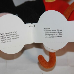 Puede incluir: Etiquetas blancas de cuidado y precauci&oacute;n adjuntas a un juguete de peluche de Mickey Mouse. La etiqueta de cuidado indica que se debe limpiar la superficie con agua tibia y jab&oacute;n suave, secar al aire y cepillar para restaurar la apariencia del tejido de felpa. La etiqueta de precauci&oacute;n indica que se debe quitar completamente la etiqueta y desechar las piezas de sujeci&oacute;n antes de dar el juguete a un ni&ntilde;o. La etiqueta tambi&eacute;n incluye el texto "THE WALT DISNEY COMPANY".