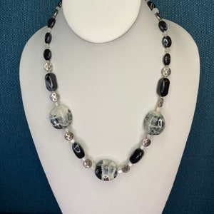 May include: A black and white necklace with oval and round beads. The necklace is made with black and white agate beads and silver spacer beads.