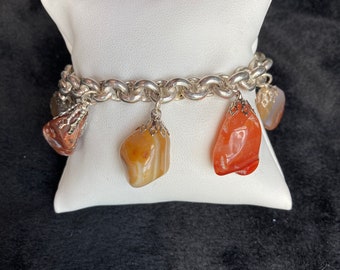 Pode incluir: Um bracelete de corrente de prata com três pingentes feitos de pedras de ágata laranja, marrom e vermelha.