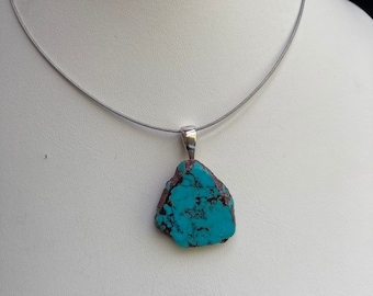 May include: A turquoise pendant necklace with a silver chain. The turquoise stone is a natural, irregular shape with brown veins.