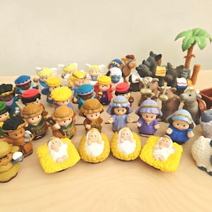 May include: A collection of plastic nativity figurines including various human characters in robes, angels, a camel, a donkey, sheep, and a palm tree. Several figures are depicted as infants in yellow plastic mangers, and a small brown cart is included.