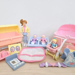 Puede incluir: Un conjunto de accesorios de casa de muñecas de plástico que incluye un cochecito amarillo y melocotón, un moisés rosa, un carrito pequeño, un caballito balancín, un teléfono, una bandeja de alimentación, una manta blanca y una muñeca.